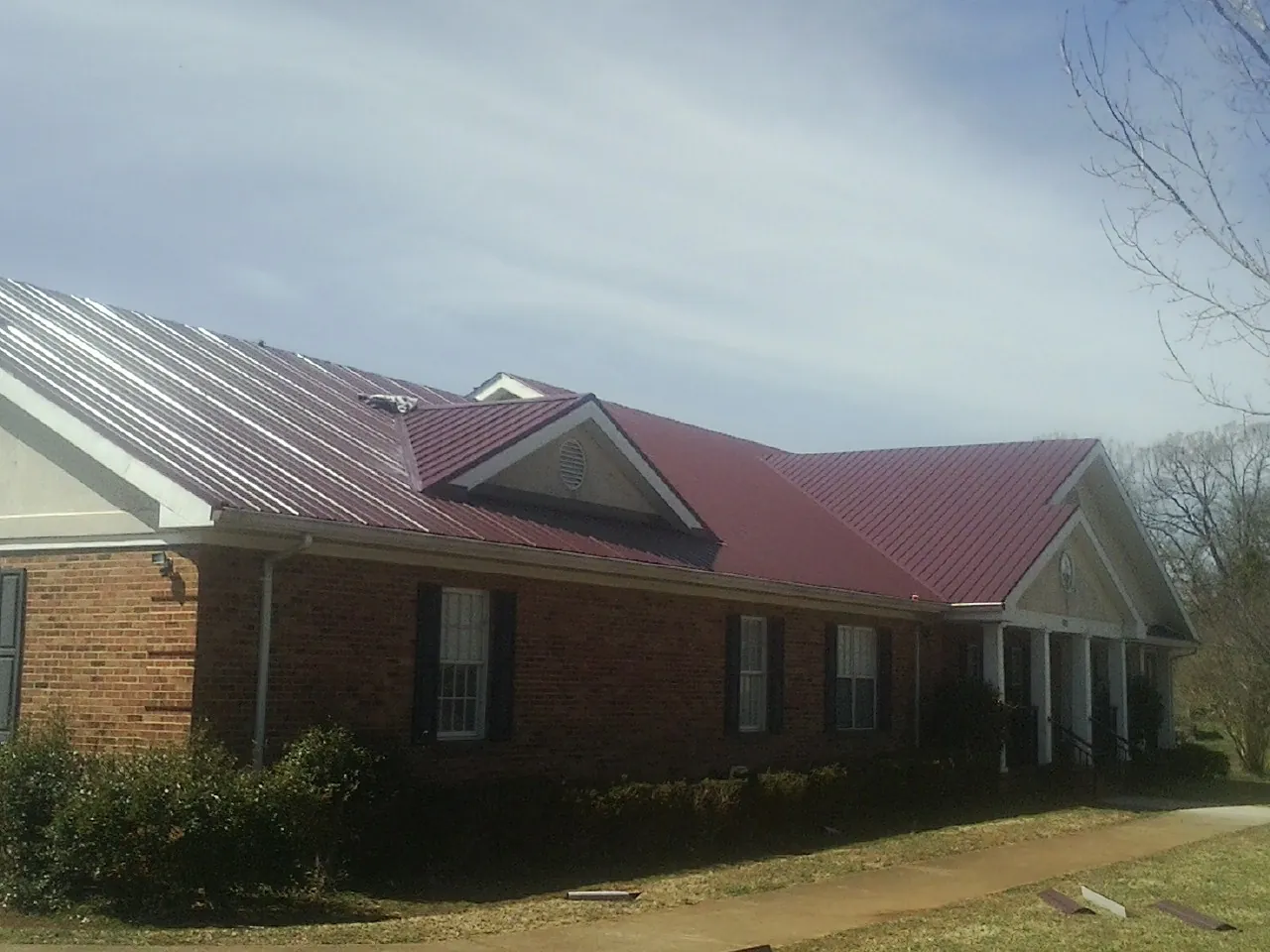 Red metal roof with gabled entries on a long brick building, from a Hail Damage Roof Repair job in Benton City