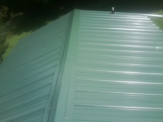 New green metal panels meeting at the ridge of a roof — Flat Roof Repair work by our crew in Benton City