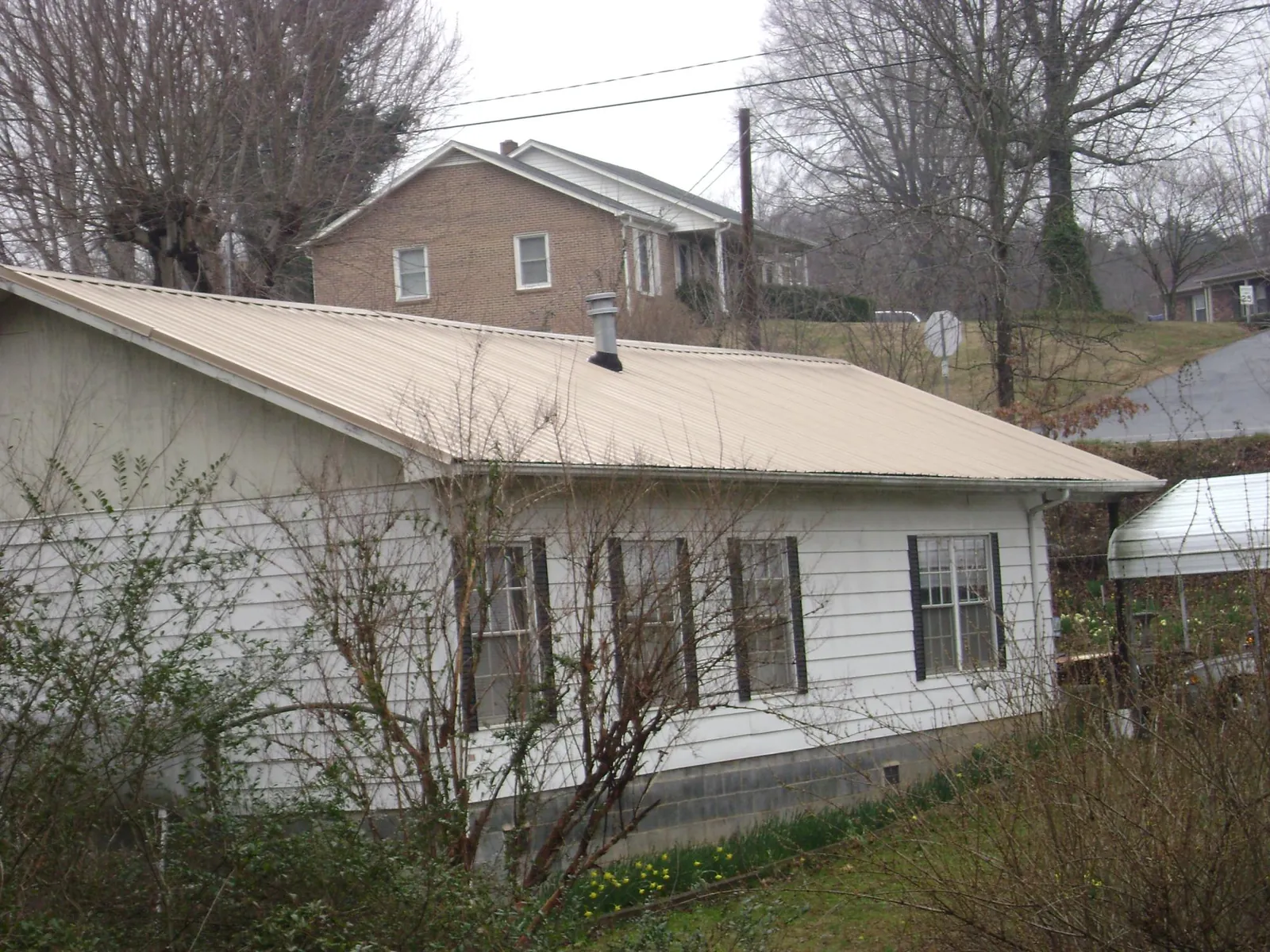 Tan metal roof on a white sided house set into a hillside — Commercial Roofing by Roofing Brothers in Benton City